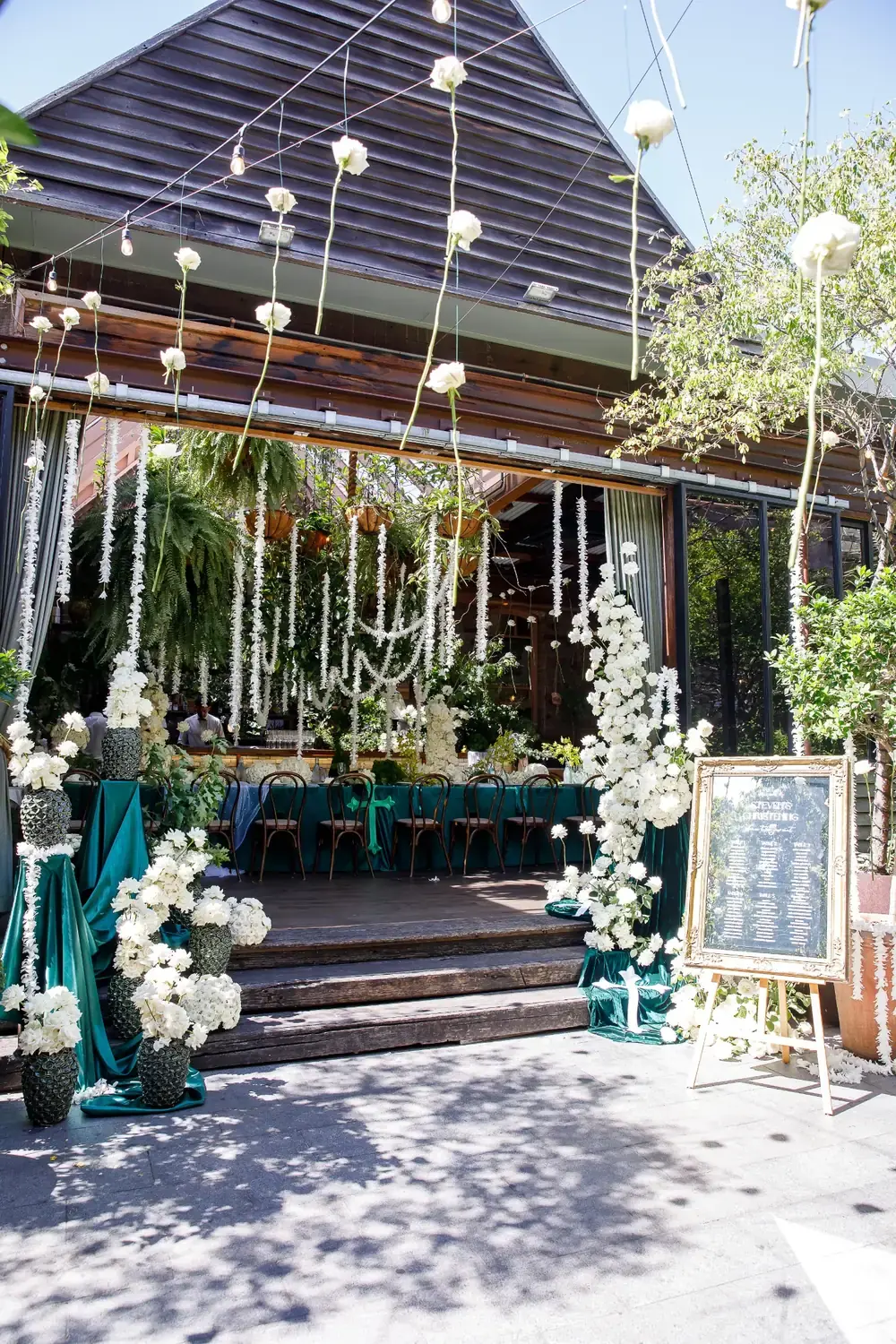 Outdoor christening setup with hanging white flowers, greenery and styled floral welcome display