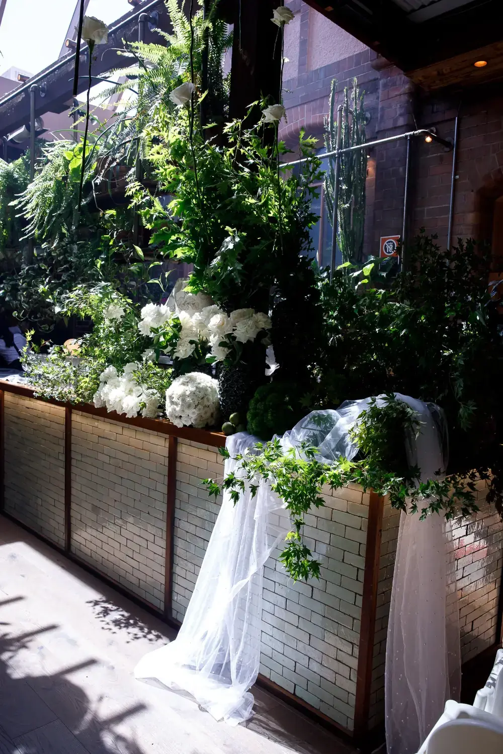 Christening floral display with white roses and greenery styled along venue bar with draped fabric